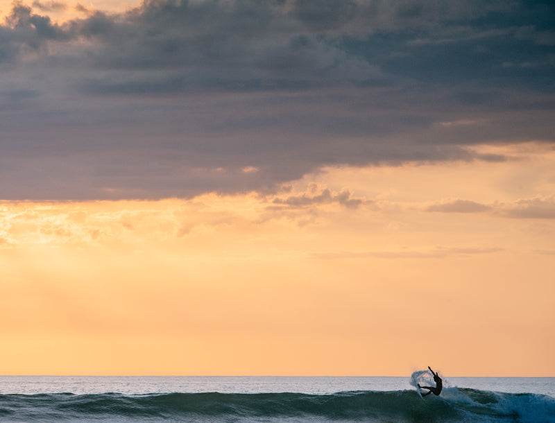 Surfer catching a wave during a pretty sunset in Tamarindo Costa Rica. Photographed by Kristen M. Brown, Samba to the Sea for The Sunset Shop.