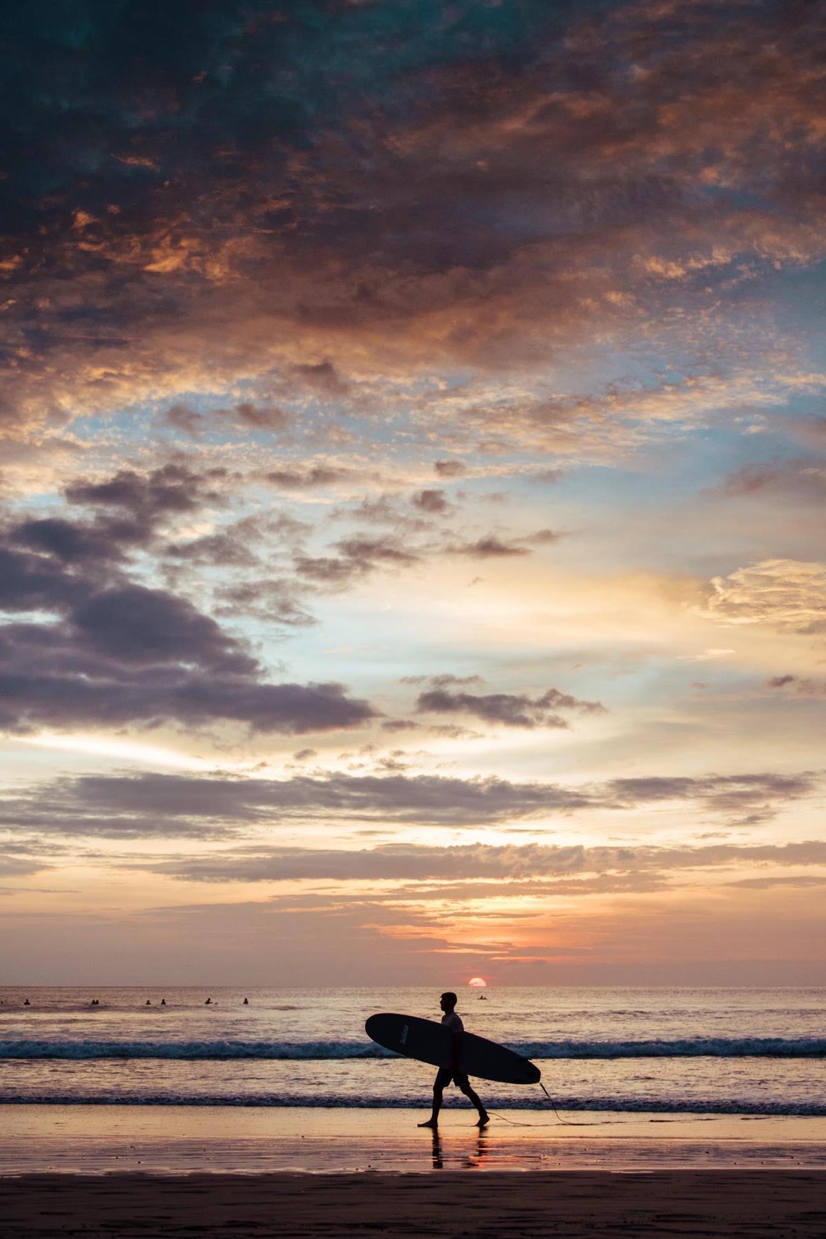 Surfer walking on the beach during sunset in Tamarindo Costa Rica. Photographed by Kristen M. Brown, Samba to the Sea. 