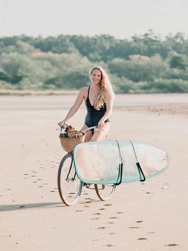 Surfer girl on the beach in Tamarindo Costa Rica riding her Schwinn bike, Nantucket Bike basket, and longboard. Kristen M. Brown, Samba to the Sea for The Sunset Shop.