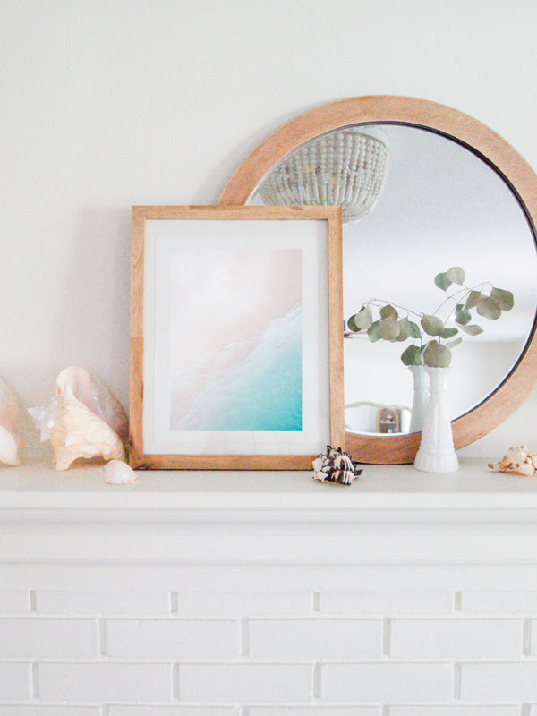 Coastal white fireplace with shells and aerial beach print. Aerial image of white sandy beach and turquoise ocean in Playa Conchal, Costa Rica. With the days merging together, the sun caressing your face, and the warm ocean touching your soul, you could be in Costa Rica, Hawaii, St. Barths, or around the world in Fiji. It doesn't matter, it's your paradise. Photographed by Kristen M. Brown, Samba to the Sea for The Sunset Shop.