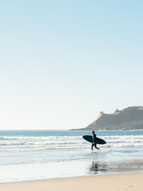 Surfer walking into the ocean in Cape Kiwanda, Oregon. Photographed by Kristen M. Brown of Samba to the Sea for The Sunset Shop. "Into the Blue" Oregon Coast surfer photo print.