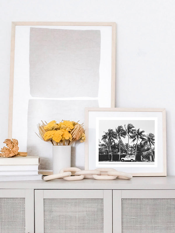 Black and white photo print of a vintage Land Rover Defender parked in front of palm trees in Palm Beach, Florida. Natural wood framed vintage Land Rover photo print paired with geometric art in a neutral, coastal casual living room with dried flowers and wood chain.. Land Rover photo print by Kristen M. Brown of Samba to the Sea, available at The Sunset Shop.