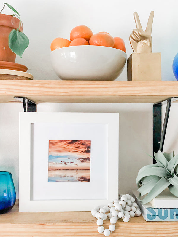 Surfer sunset shelfie print on open shelving. Surfer walking on the beach during a beautiful sunset in Costa Rica. Sunset surfer print by Samba to the Sea at The Sunset Shop. “Where the Sky Meets the Sea” surfer sunset print by Kristen M. Brown, Samba to the Sea. Styled by Southern Mesa Trading.