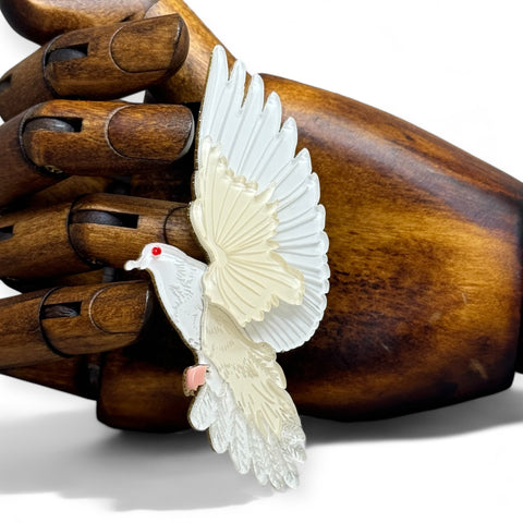 Image of an acrylic art brooch of a dove in flight set against an artists wooden hand for scale