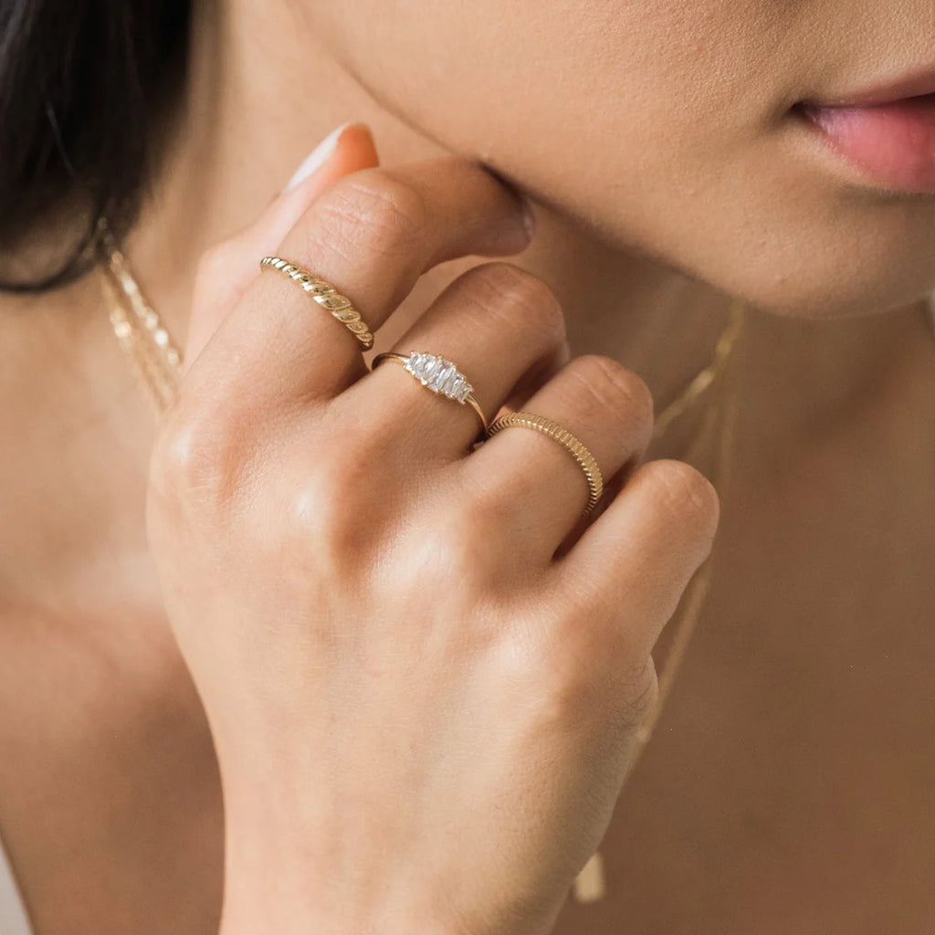 Woman wearing three gold rings on one hand: Croissant Ring, Baguette Cluster Ring, and Ribbed Stacking Ring.