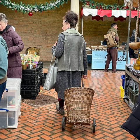A woman with a wicker shopping trolley browsing Stroud Farmers' Market stalls