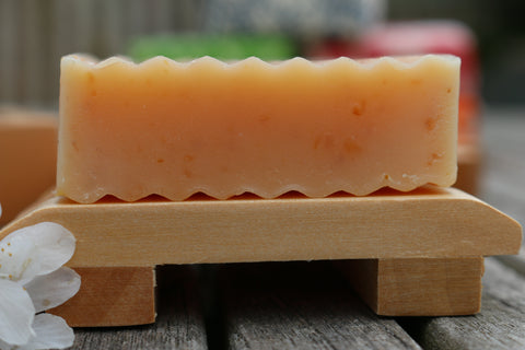 A bar of College Green amber coloured beer soap on a wooden soap dish