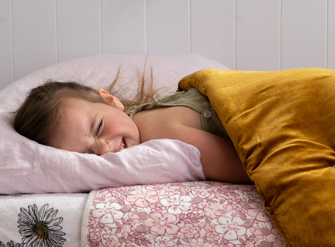 little girl lying on a pillow in a pink bed with bed mates