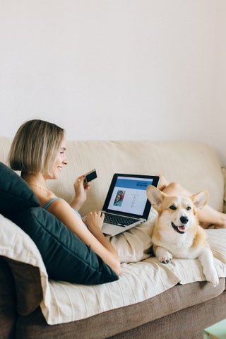 A woman sitting on couch with her dog shopping online