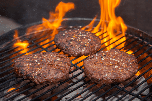 three ostrich burger patties on a charcoal grill