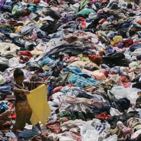 Sea of discarded clothing in landfill with small child picking through it