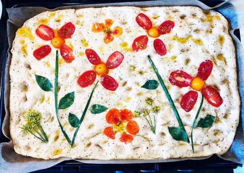 Uncooked focaccia with toppings arranged into flower patterns