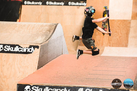 A rider does a bri flip on his scooter on the long and low at Rampfest Indoor Skatepark