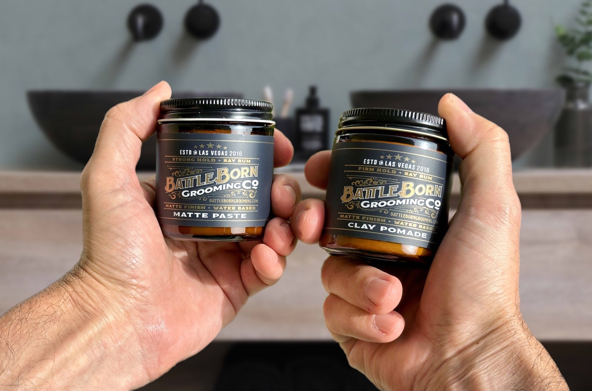 Photo of Two Jars of Natural Hair Styling Products - Clay Pomade and Matte Paste - with Person Deciding Which to Use for Their Hairstyle