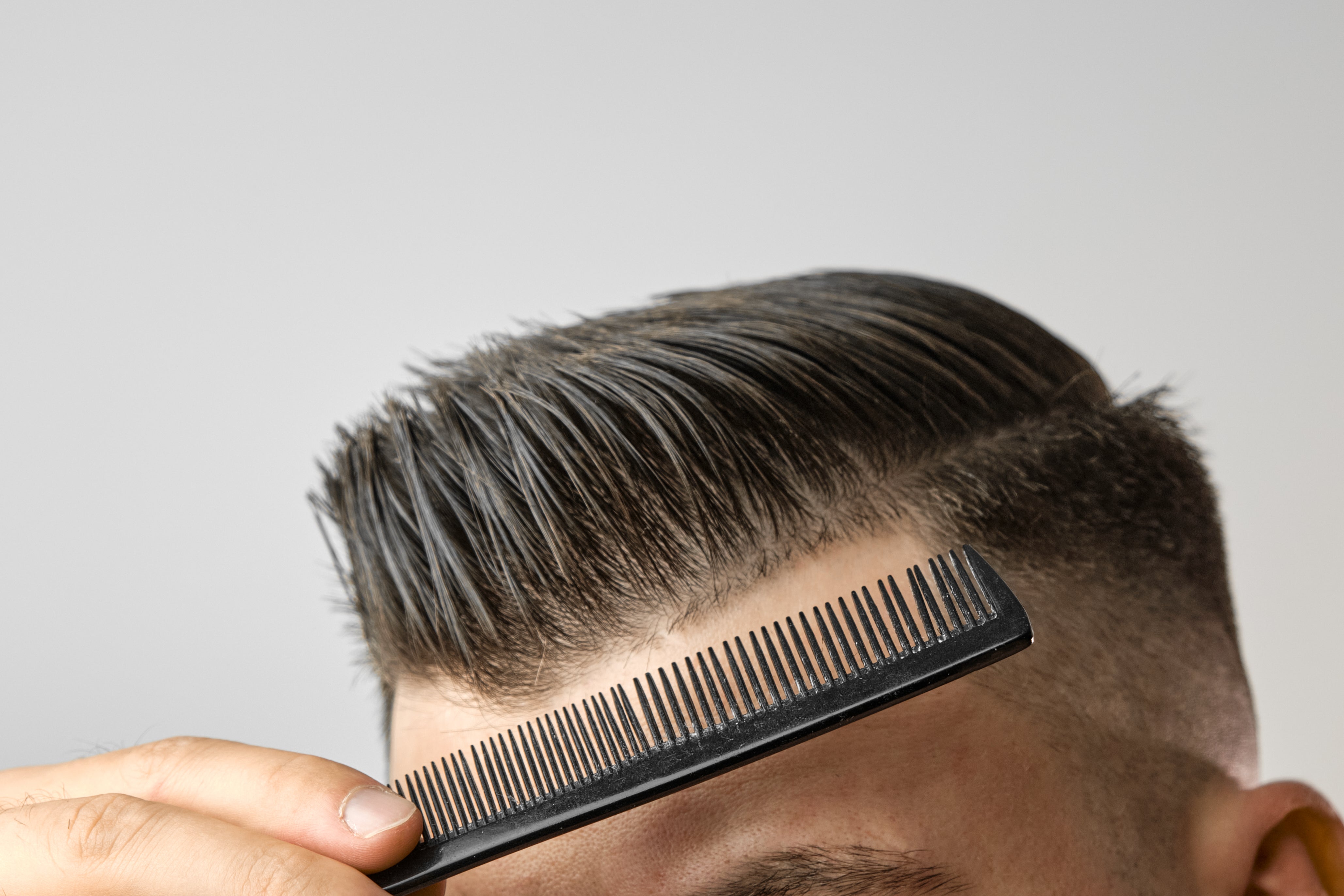 A close-up view of a man's hair being combed, showcasing the glossy finish achieved using hair pomade.