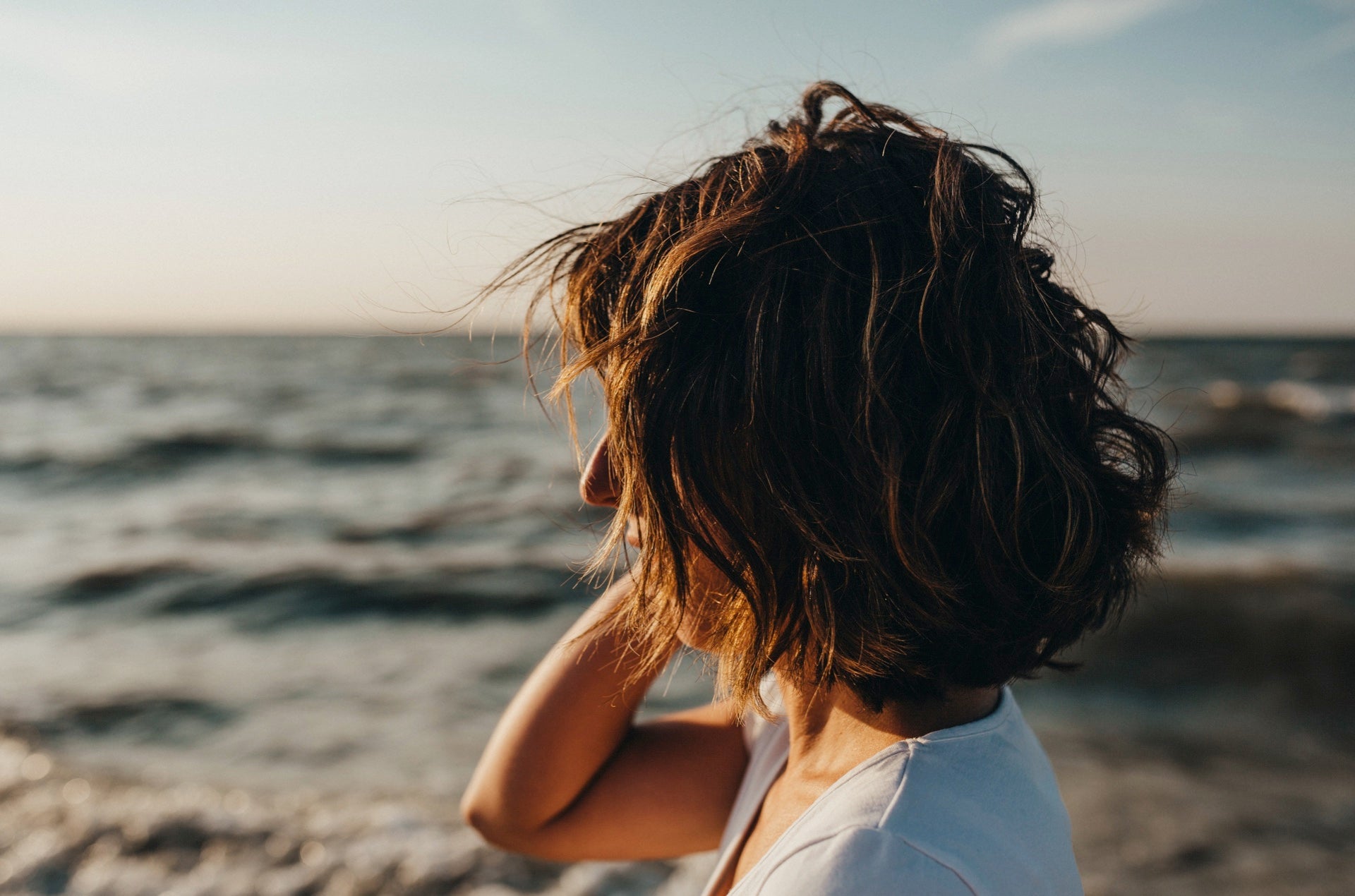 A girl with beach hair standing at the beach, windswept and relaxed, embodying the essence of summer and ocean vibes. Photo by Xavier Mouton Photographie on Unsplash