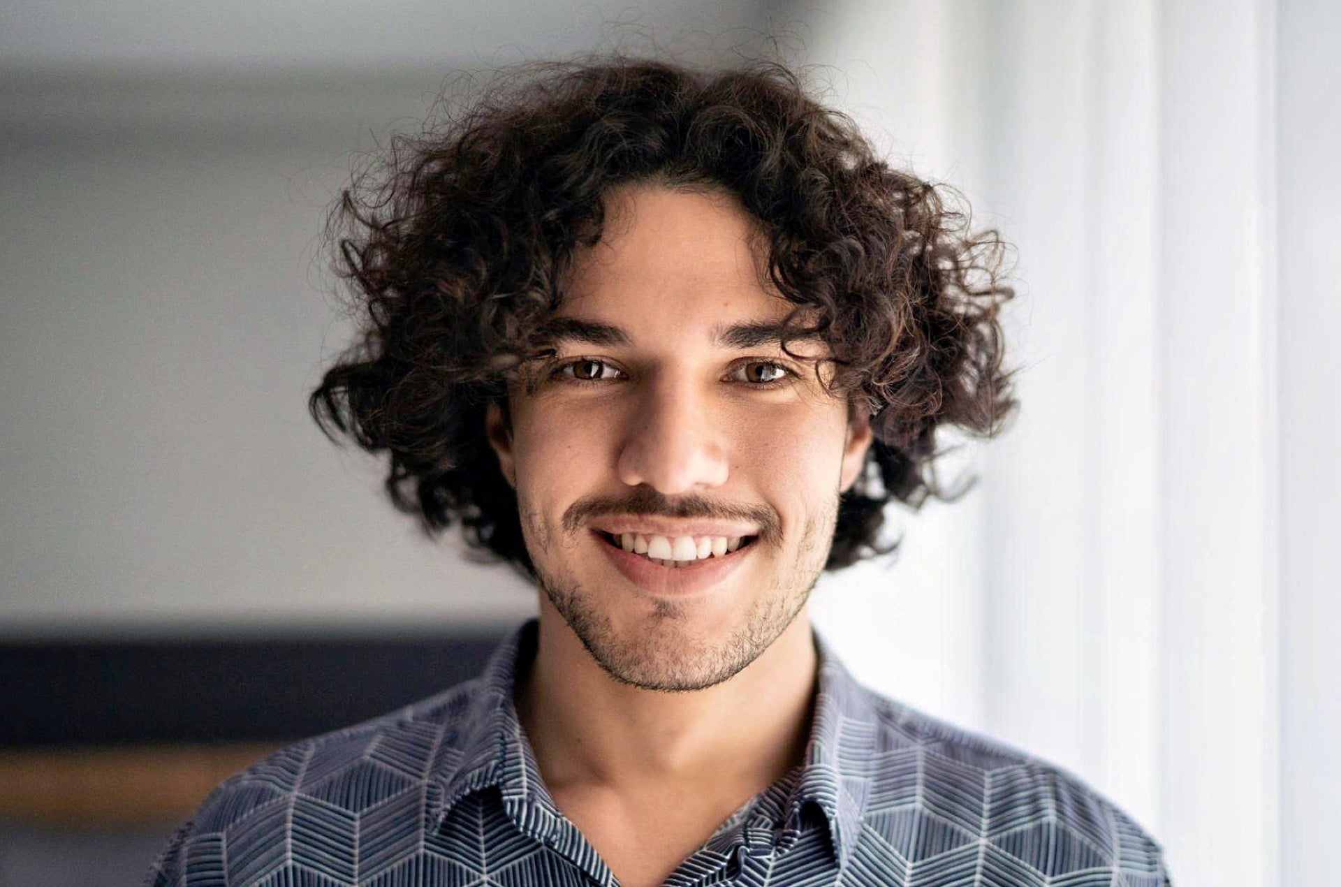 A smiling man with short, curly hair, encouraging viewers to question, "what is my hair type?" while exemplifying a curly hair type.