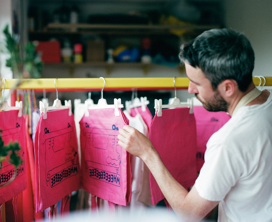 Patrick looking through a yellow rail of pink tote bags