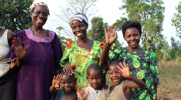 Ugandan women and children smiling and waving.