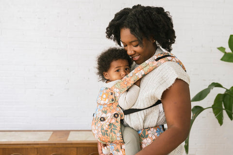 A mother being close to her child that is sitting in a Tula Baby Carrier.