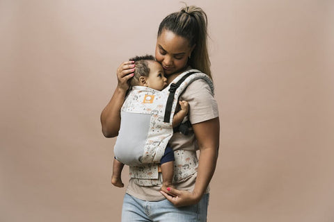 A mother carrying her child in a baby carrier.