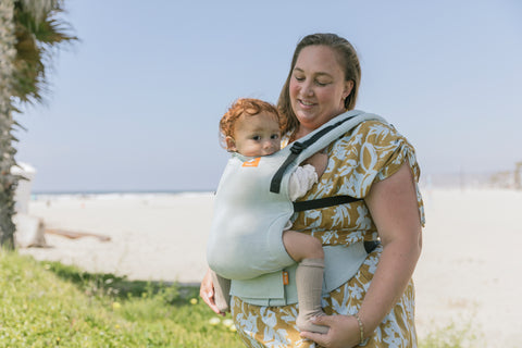 A mother wearing her baby in a Linen Carrier in summer, while standing in the shade.