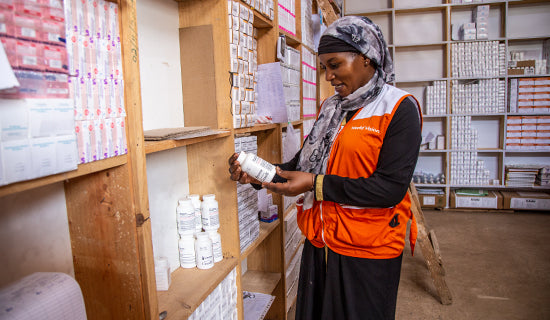 A volunteer stands inside a stocked pharmacy, reading the side of a pill bottle.