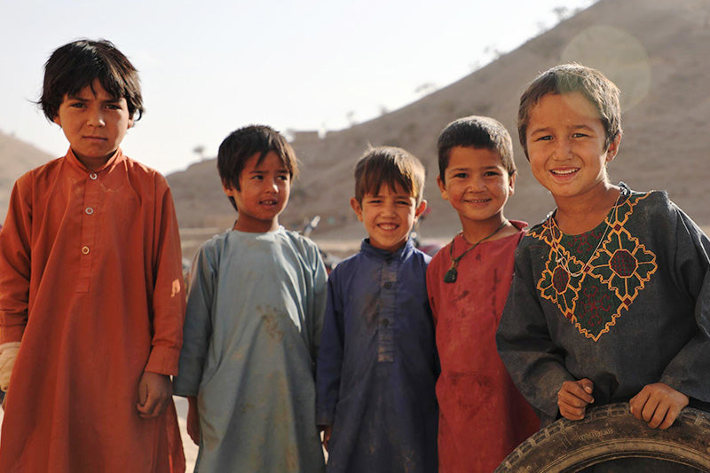 In Afghanastan five boys stand together in robes and smile.  