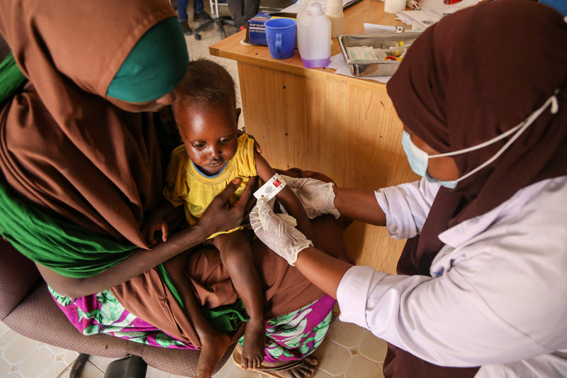 In Somalia, a young child sits on his mother's lap as a nurse measures his arm. 