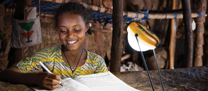 A solar light lights up a room as a young girl studies writing on a notebook.