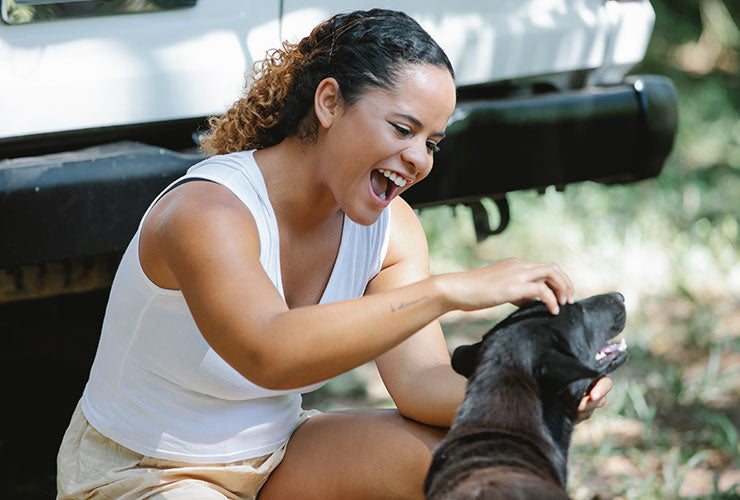 Smiling Young Woman Playing With Dog Outside Next to Car