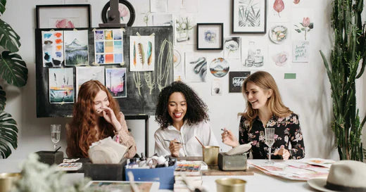 Drei Frauen, die an einem kreativen Arbeitstisch gemeinsam Spaß haben symbolisieren eine Gemeinschaft aufbauen