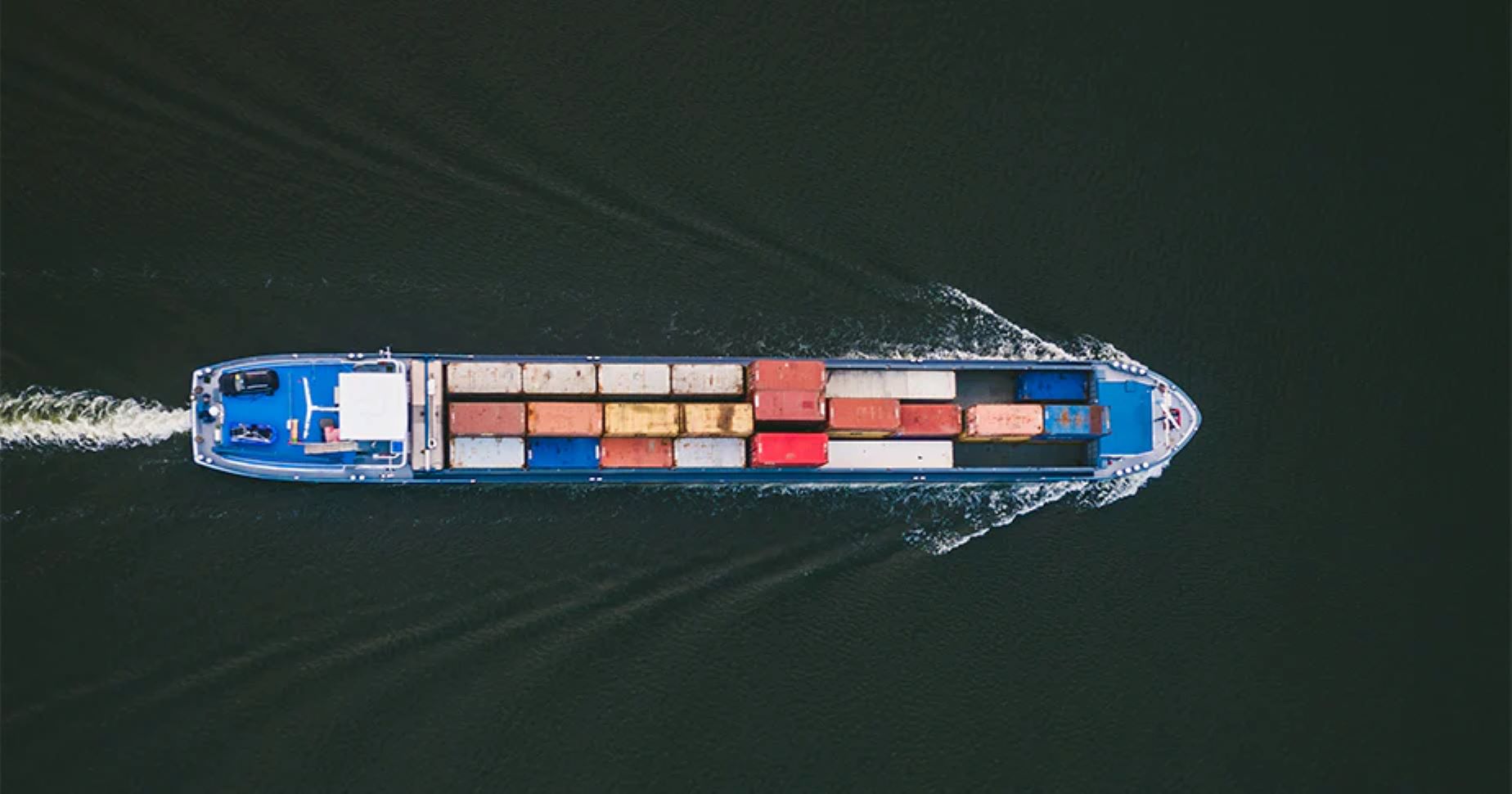 Gezeigt ist ein Schiff von oben. Auf dem Schiff sind zahlreiche Container gelagert.