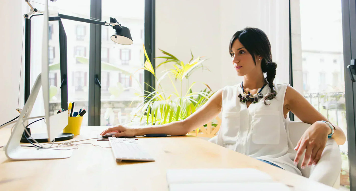 Eine dunkelhaarige Frau sitzt am Schreibtisch vor ihrem Computer.