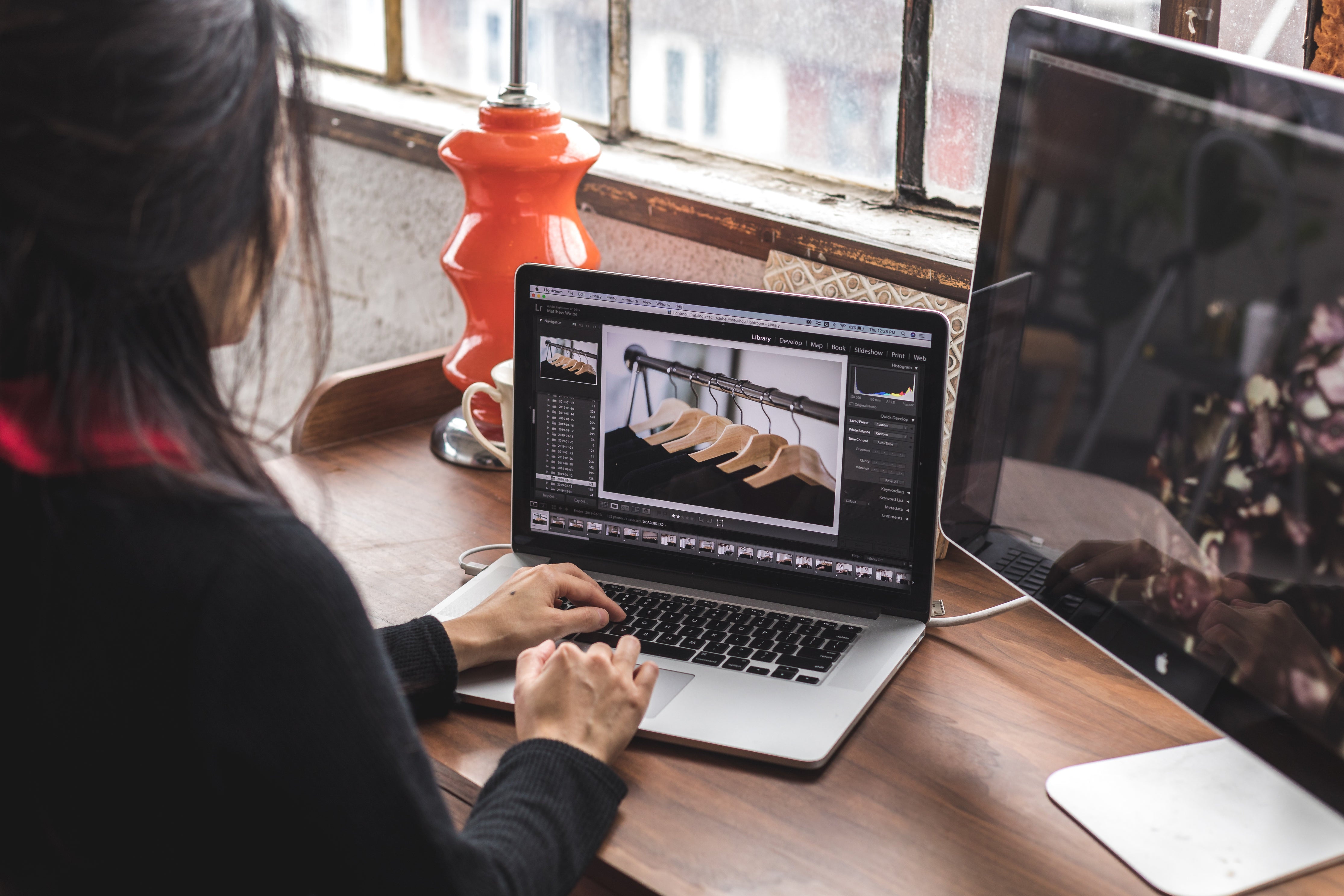 Blick über die Schulter einer jungen Frau, die an einem Schreibtisch vor einem Laptop und einem Desktop-Bildschirm sitzt und arbeitet. Direct-to-Consumer (D2C) ist zwar nichts Neues, im E-Commerce aber gerade der Renner. Wir zeigen dir, wieso!