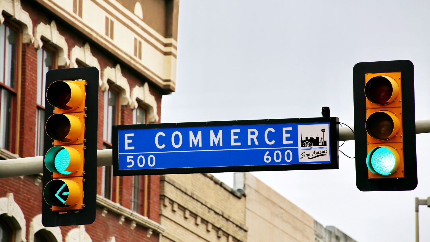 Gezeigt sind zwei Ampeln, zwischen denen ein Straßenschild hängt. Auf dem Schild steht „E-Commerce“.