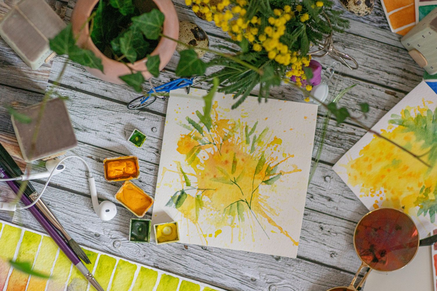 Das Bild zeigt einen Tisch, auf dem ein Wasserfarbbild von einer gelben Blume liegt.