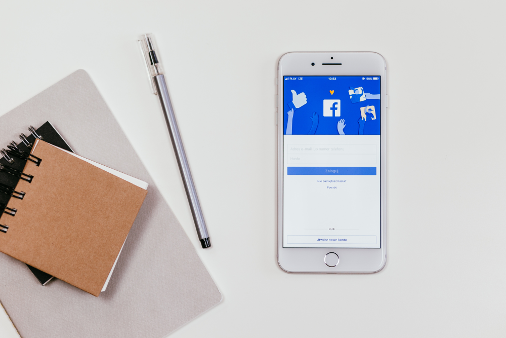 Ein Blog und ein Stift liegen links neben einem Handy mit der Facebook Anmeldeseite.