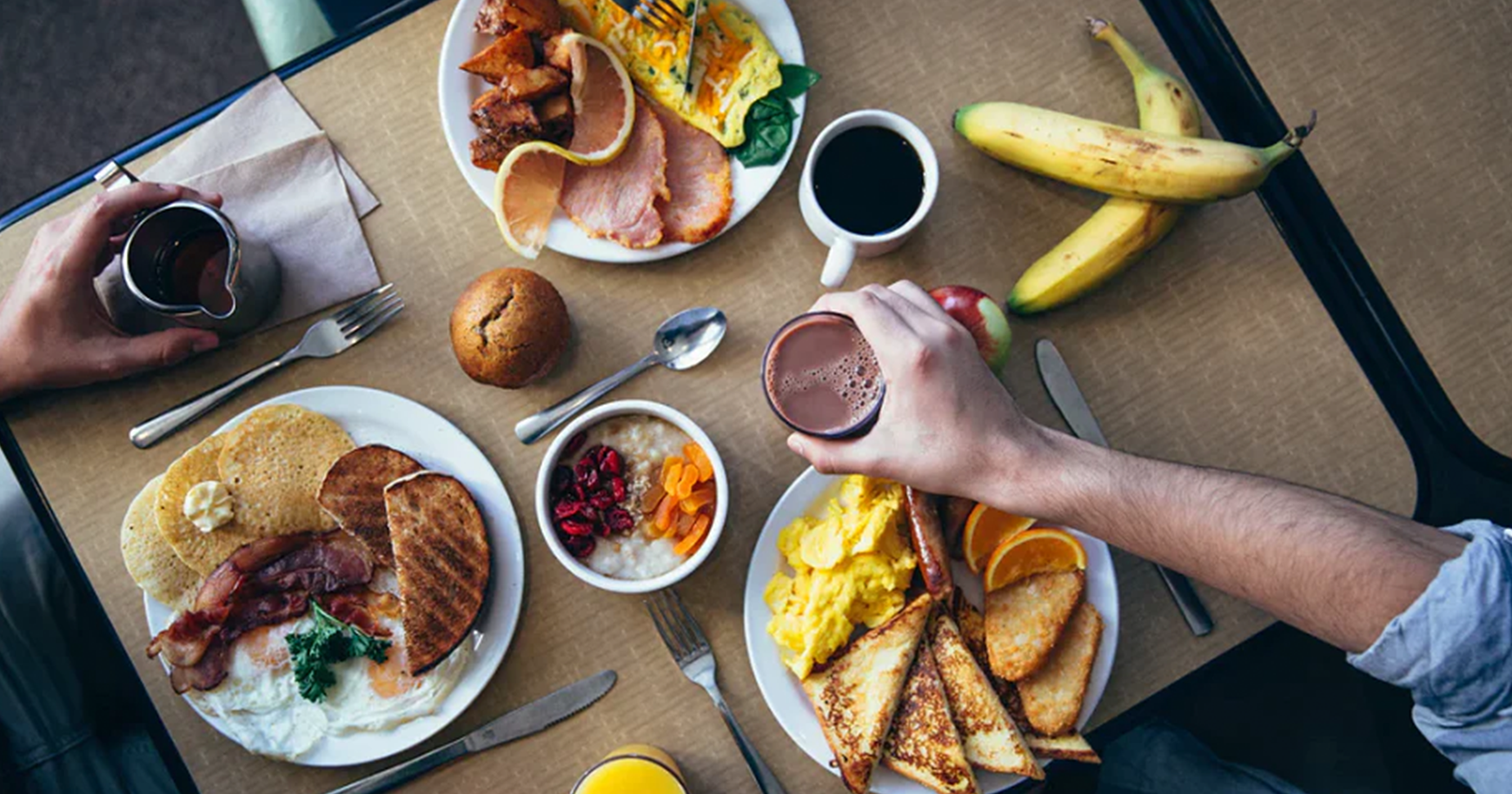 Ein gedeckter Tisch mit drei Teller, die mit Frühstück wie Toast, Ei und Speck gefüllt sind.