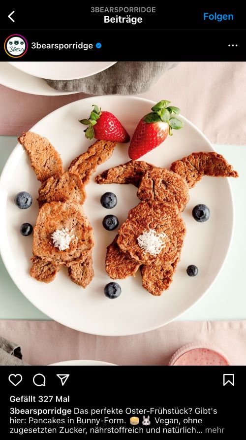 Ein Teller, auf dem zwei hasenförmige Pancakes sowie Blaubeeren und zwei Erdbeeren liegen.