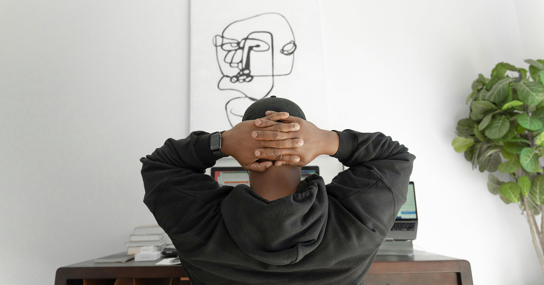 Das Foto zeigt eine Person von hinten, die an einem Schreibtisch sitzt und die Hände über dem Kopf zusammenschlägt.