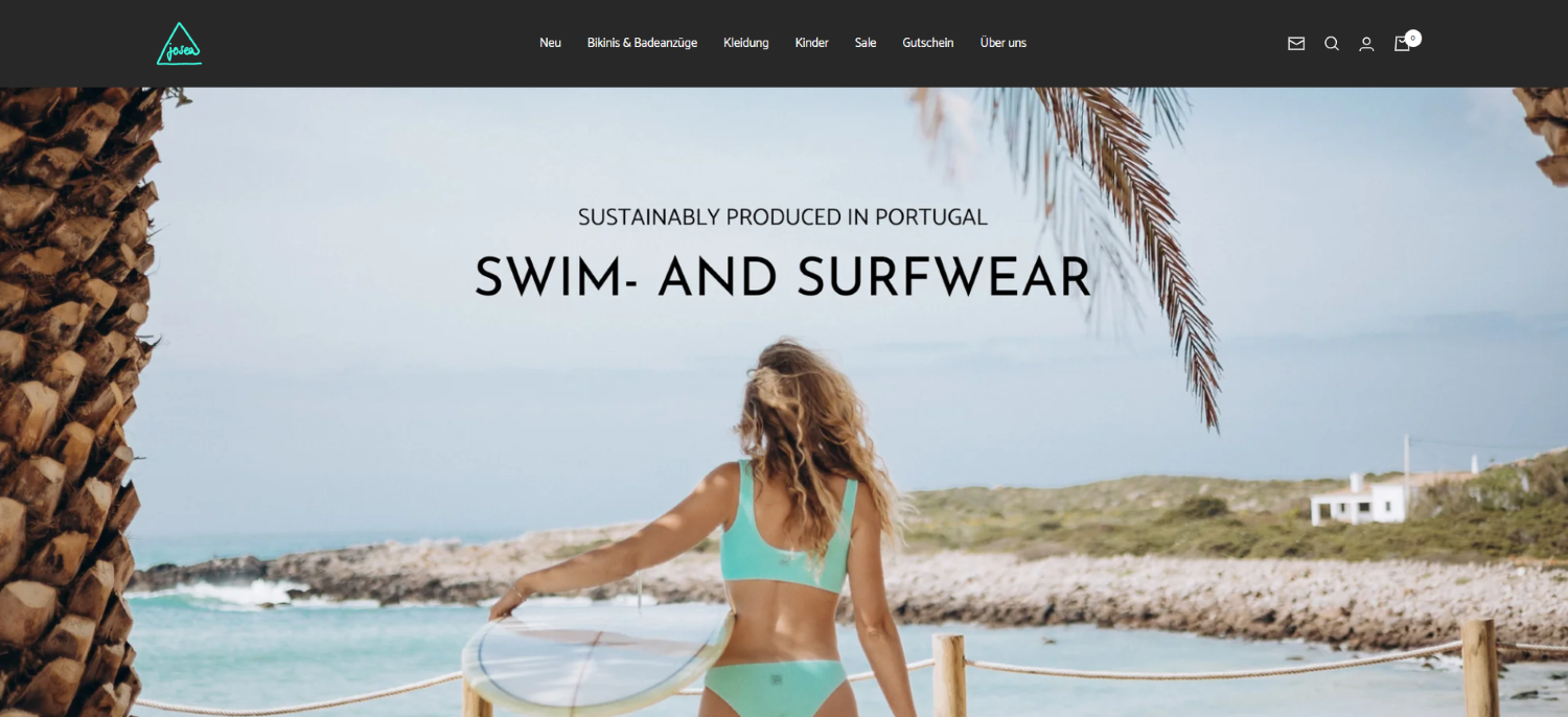 Das Bild zeigt die Website von Josea Surfwear. Zu sehen ist eine Frau, die in einem Bikini am Strand steht und ein Surfbrett in der Hand hält.