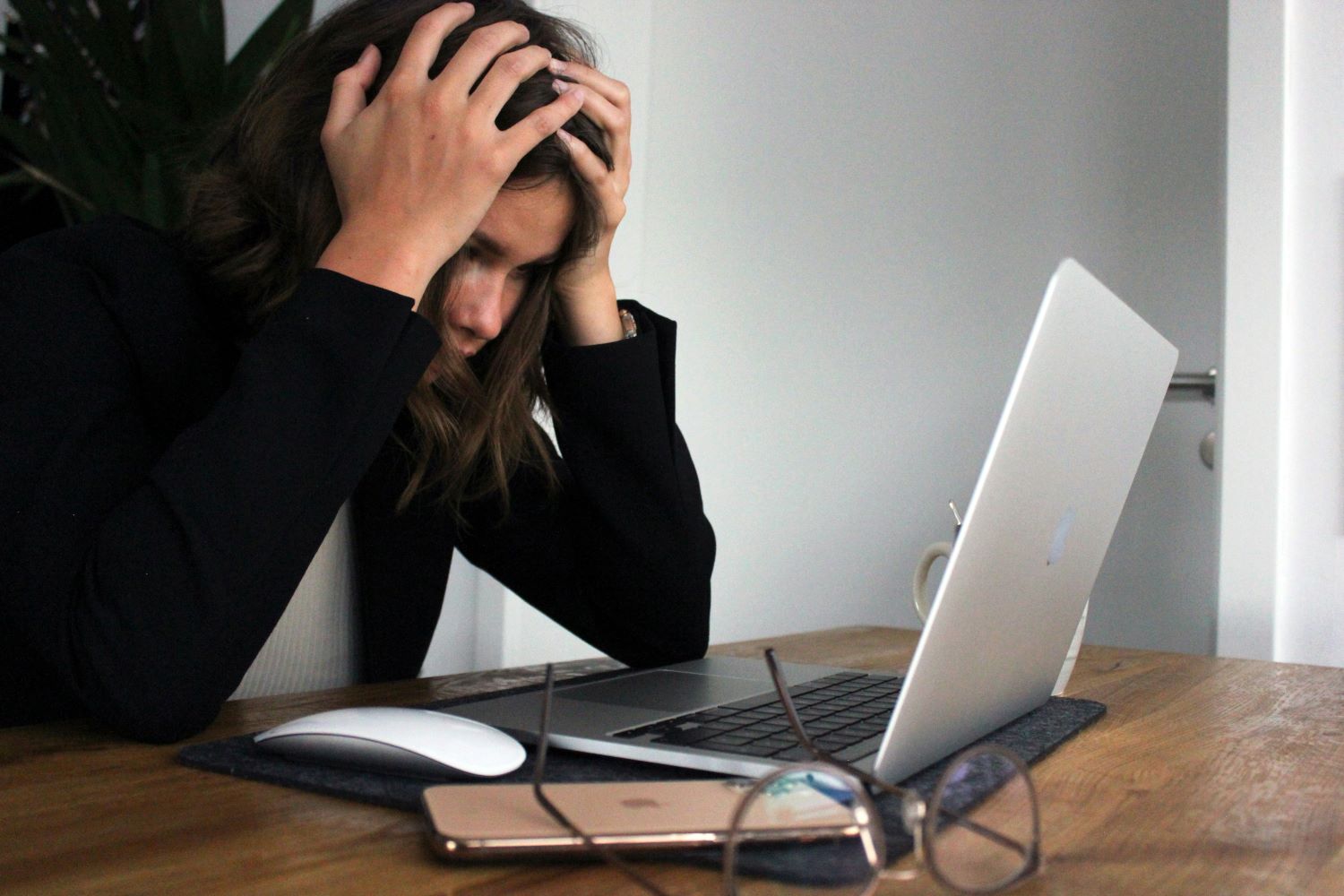 Zu sehen ist eine Frau, die vor einem Laptop sitzt und die Hände über dem Kopf zusammenschlägt.