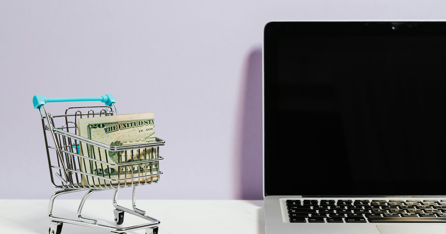 Onlineshop kaufen oder Onlineshop verkaufen: Ein kleiner Einkaufswagen mit einer 20-Dollar-Note, der neben einem Laptop steht