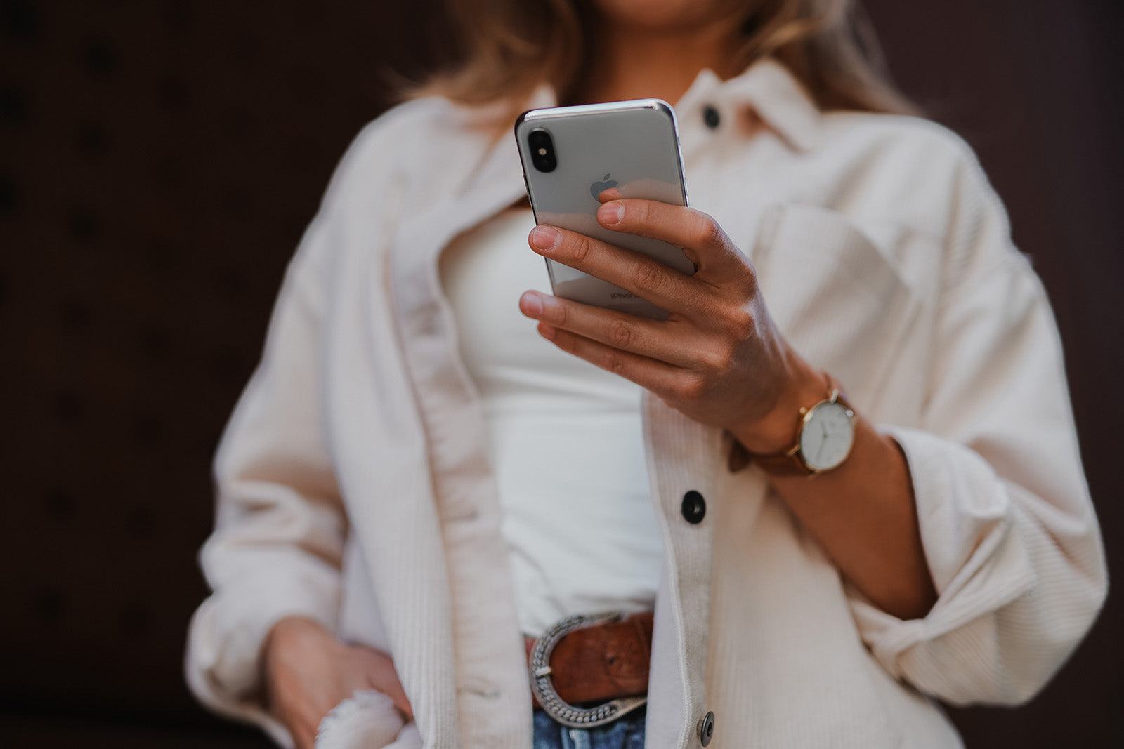 Eine Frau in einem weißen Outfit betrachtet auf einem Handy eine After-Sales-Management-Kampagne