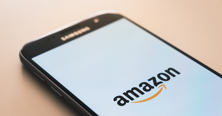 Das Foto zeigt ein Smartphone, das auf einem Tisch liegt. Auf dem Bildschirm leuchtet das Amazon-Logo auf. Wir zeigen dir im Blogbeitrag, wie du auf Amazon verkaufen kannst.