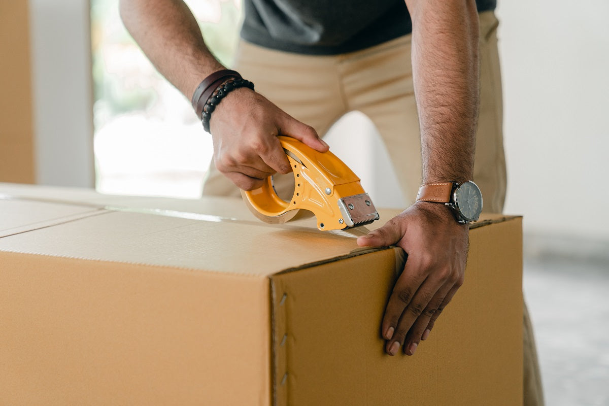 Ein Mann verschließt ein Paket mit Klebeband. Erfahre, wo der Unterschied zwischen Bestellverwaltung und Auftragsmanagement liegt.