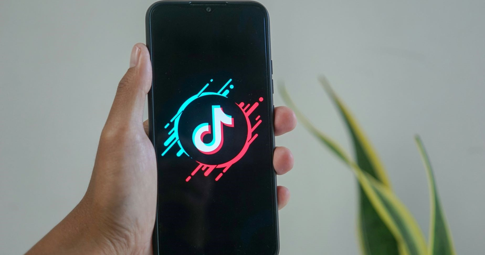 Zu sehen ist eine Hand in der ein Smartphone gehalten wird. Auf dem Smartphone ist das TikTok Logo zu sehen.