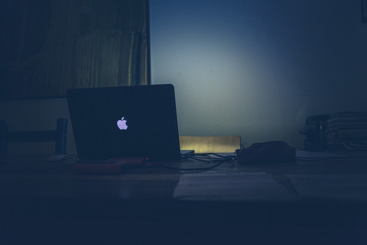 Das Foto zeigt einen dunklen Raum, der durch das leuchtende Apple Logo auf einem Laptop erhellt wird. Apple nutzt Branding um seine Marke einzigartig zu machen.