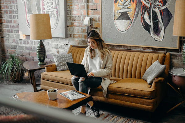 Geld verdienen mit Instagram: Eine Frau, die als Affiliate arbeitet sitzt auf einer gelben Couch und hat ihren Laptop auf dem Schoß